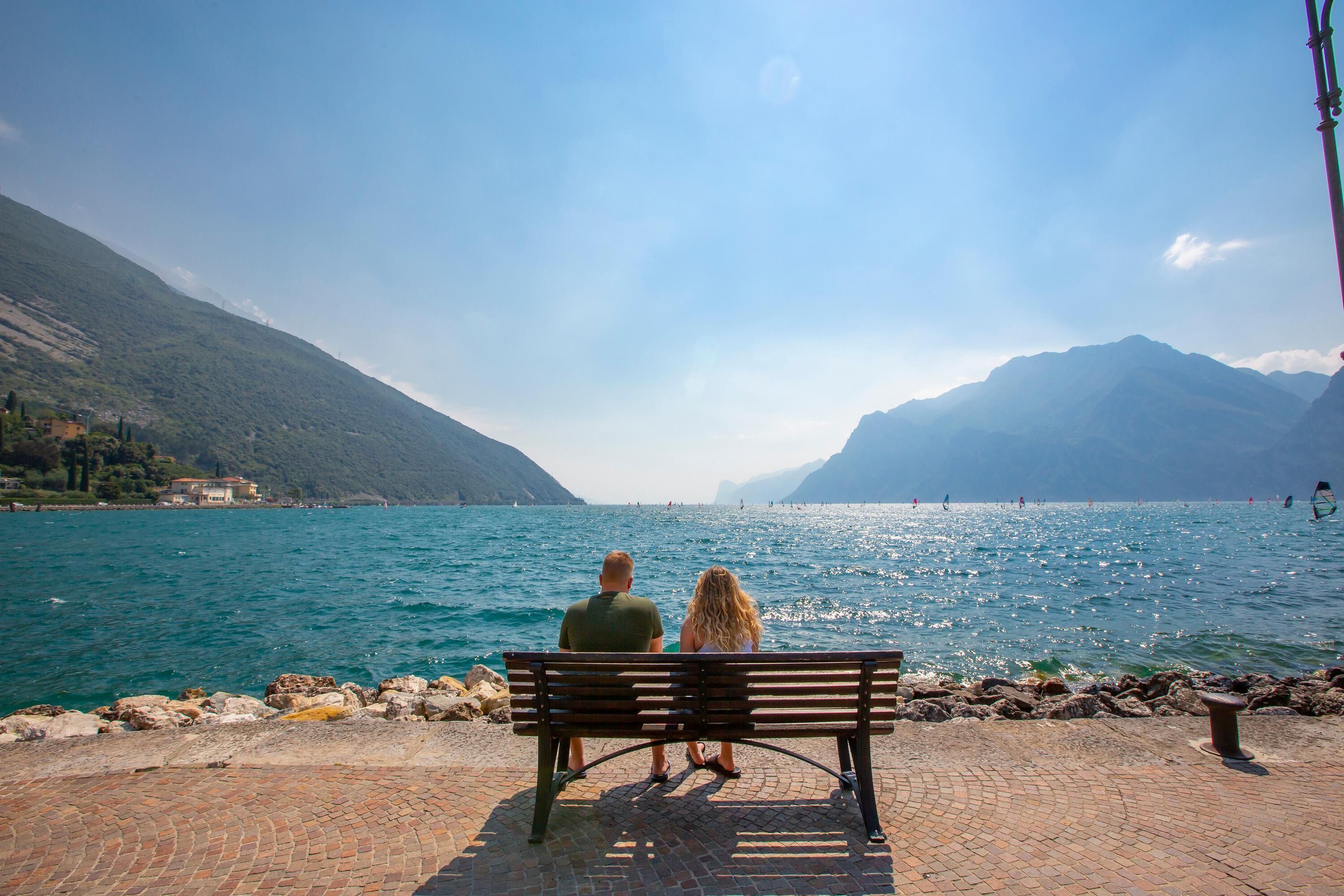 Una pareja sentada en un banco con vistas a un lago, con montañas al fondo.