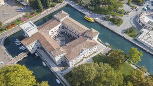 An aerial view of a historic building with a central courtyard, adjacent to a canal, surrounded by greenery and a parking area. - Riva Centro Apartment (Riva del Garda)