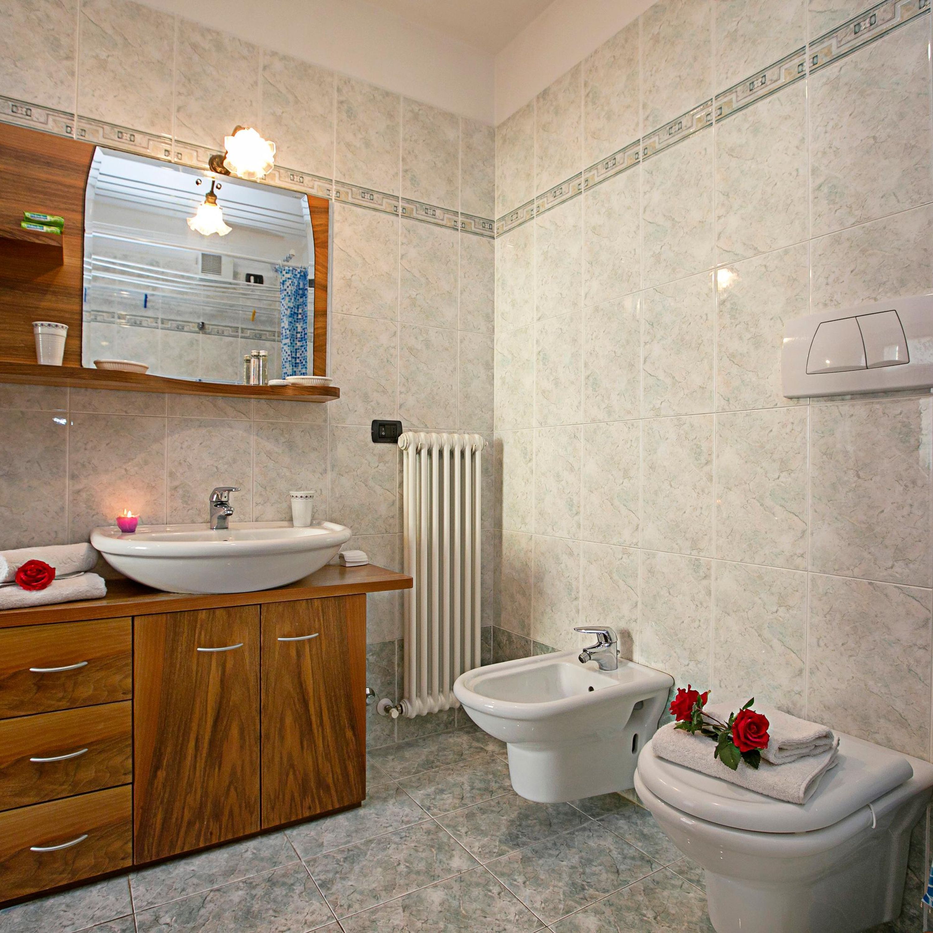 A modern bathroom with a wooden vanity, a large mirror, a sink, a bidet, and a toilet.