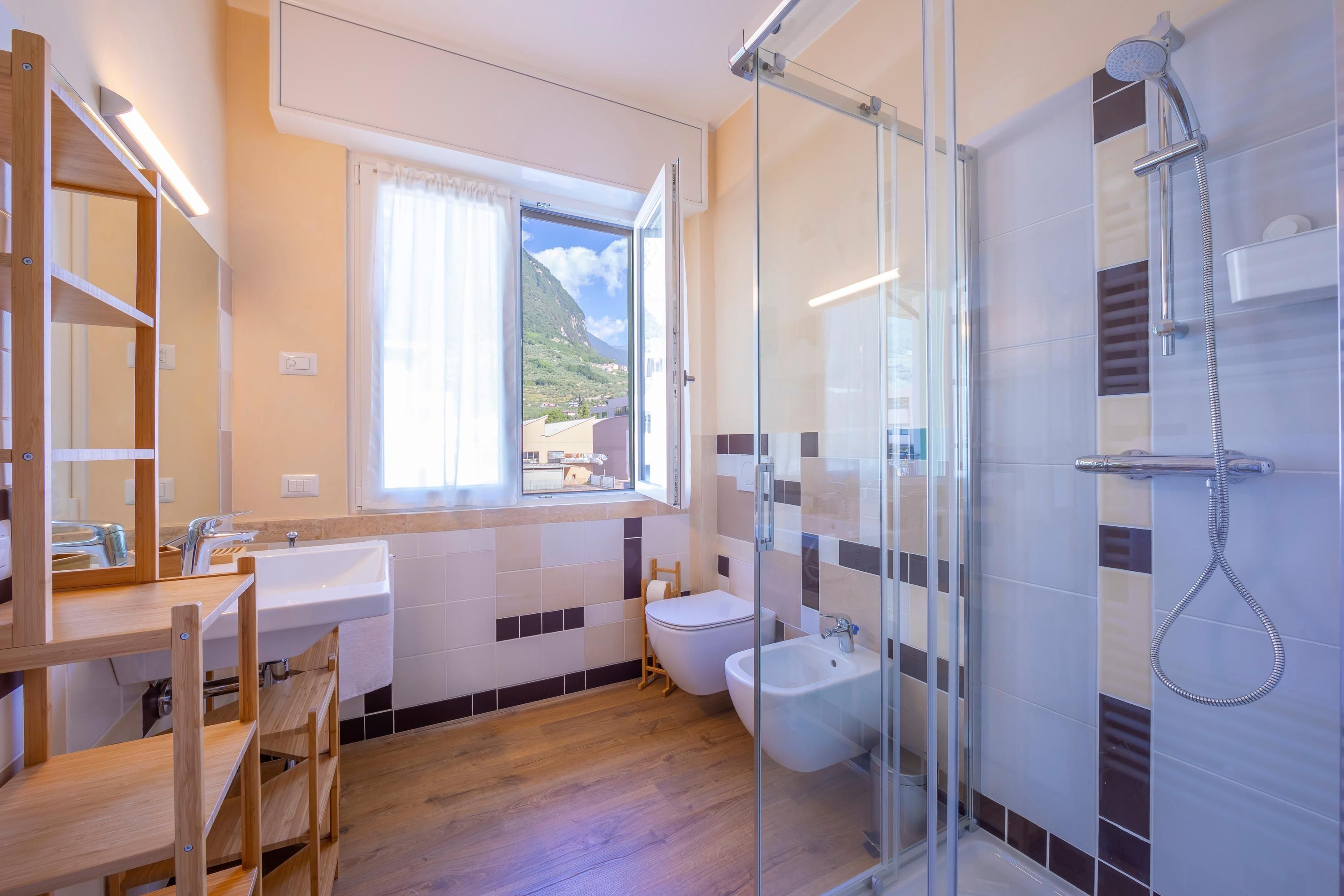A modern bathroom with a glass shower enclosure, a sink, a bidet, and a wooden vanity.