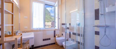 A modern bathroom with a glass shower enclosure, a sink, a bidet, and a wooden vanity.