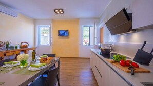 Een moderne keuken met een eethoek, een aan de muur bevestigde televisie en een houten tafel gedekt met borden en een bloevas.