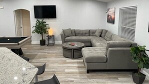 Uma sala de estar moderna com mesa de bilhar, sofá seccional, mesa de centro redonda e televisão de tela plana fixada na parede.