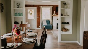 Comedor con una mesa de madera dispuesta para cuatro personas, flanqueado por estanterías blancas.
