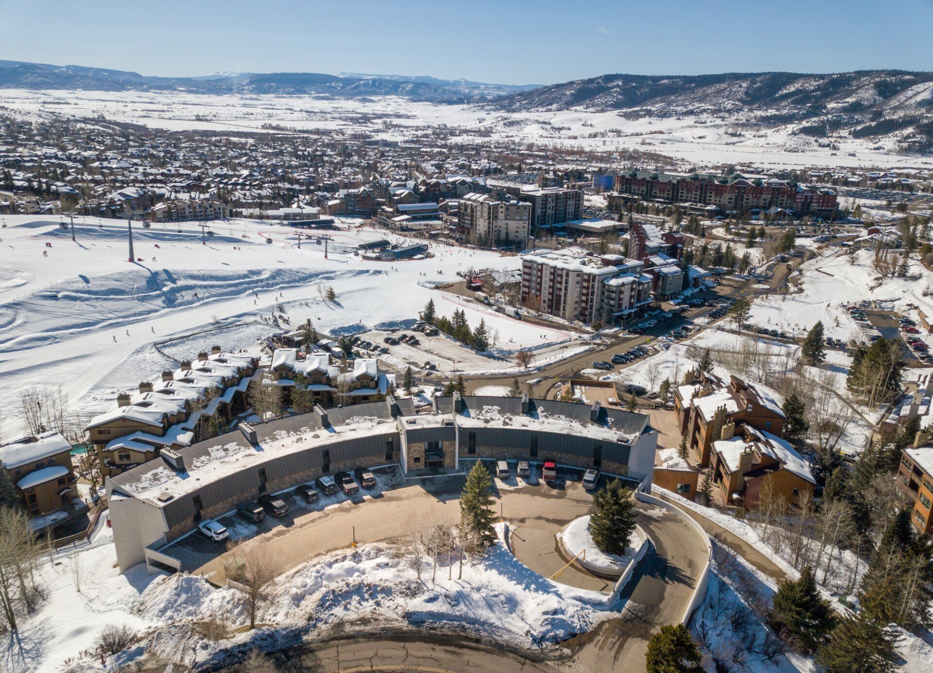 Un centro de esquí con un amplio estacionamiento, varias edificaciones y un paisaje cubierto de nieve.