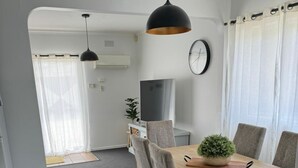 Un espace de salle à manger moderne avec une table en bois, des chaises à revêtement gris, un luminaire suspendu noir et une plante en pot.