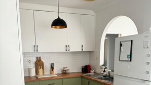 Une cuisine moderne avec des meubles blancs, un plan de travail en bois, un luminaire suspendu noir et un réfrigérateur blanc.