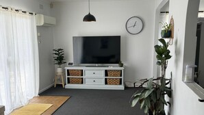 Un salon moderne avec un téléviseur à écran plat, un canapé, une table basse et une grande plante en pot.
