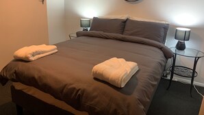 Un lit bien fait, avec deux serviettes pliées, un miroir rond accroché au mur et deux lampes de chevet.