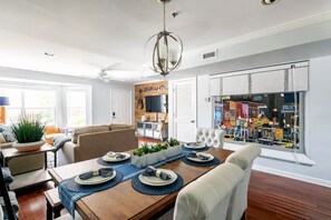 Uma sala de jantar com uma mesa de madeira posta para quatro pessoas, um candelabro e vista para a rua através de uma janela.