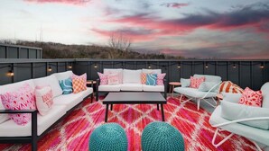 Eine Dachterrassen-Lounge mit weißer Sofagarnitur, türkisfarbenen Poufs und einem farbenfrohen roten und pinkfarbenen Teppich.