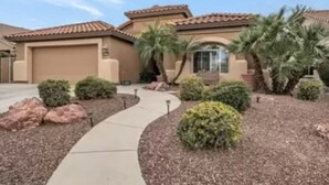 A residential house with a tiled roof, a driveway, and landscaped garden with shrubs and palm trees. - Remodeled with access to pools, pickleball, & golf in gated 55+ community! (Goodyear)