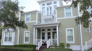 A two-story building with a front porch, a balcony on the upper floor, and a number '202' on the door.
