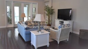 A living room with a blue sofa, white side tables, a television, and a large potted plant.