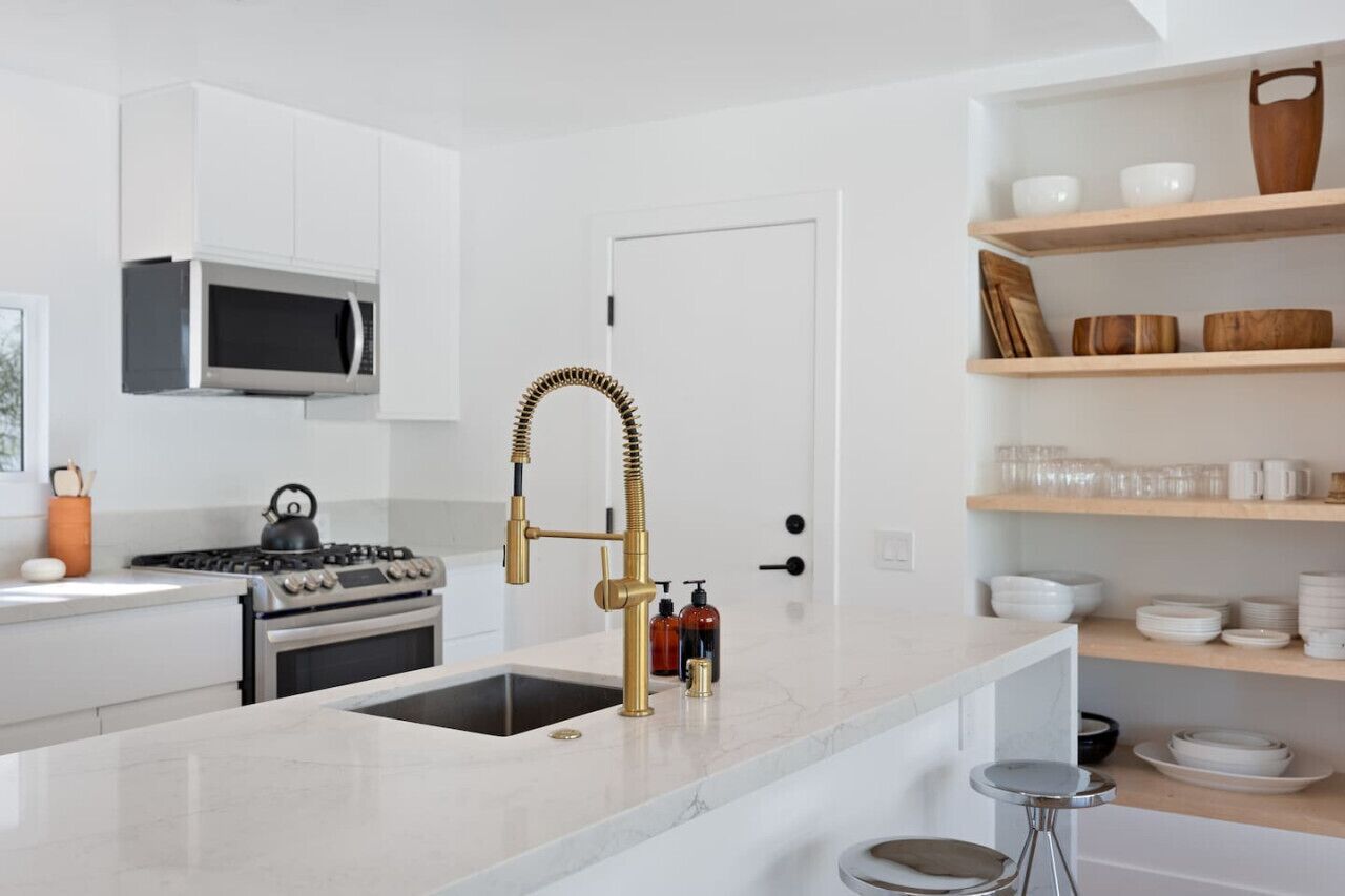 Une cuisine moderne avec des meubles blancs, une cuisinière en acier inoxydable, un robinet doré et un four à micro-ondes placé au-dessus de l’évier.