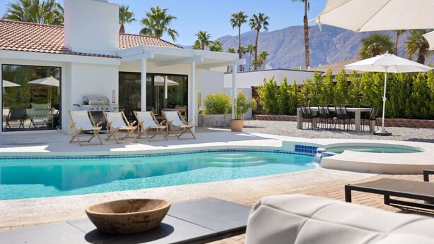 Ein moderner Poolbereich mit Liegestühlen, einem Grillplatz und Blick auf Palmen und Berge.
