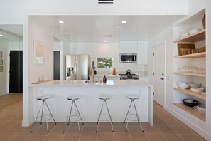 A modern kitchen with white cabinetry, a central island with stools, and a microwave above the island.