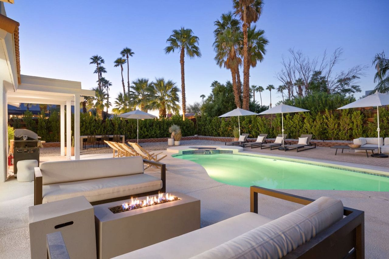 A poolside area with lounge chairs, a fire pit, and umbrellas.