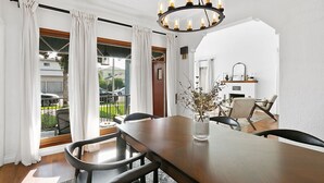 Un coin repas avec une table en bois, des chaises noires, un vase orné de branches et un lustre.