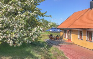 Relax in a serene outdoor setting surrounded by lush greenery and flowering trees, with a shaded dining area under a blue umbrella.