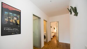 Un pasillo con un cartel a la izquierda, suelo de madera y una cama al fondo.