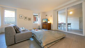 A modern bedroom with a sofa, a bed, a TV, a dresser, and a sliding glass door to a balcony. - Antico Municipio in Ponte Tresa (Tresa)