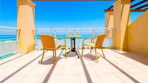Een balkon met twee rieten stoelen en een kleine ronde tafel, met uitzicht op een heldere blauwe zee.
