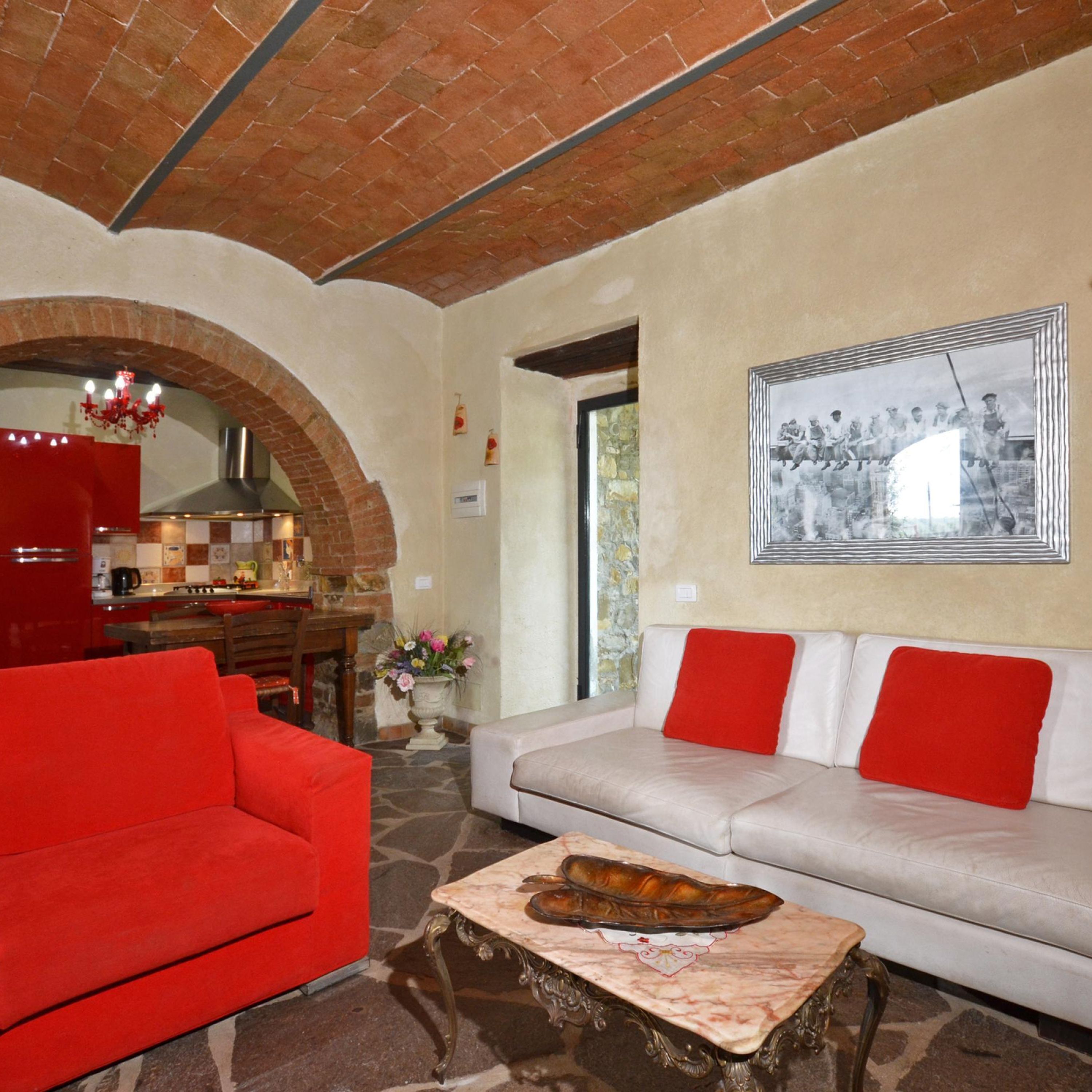 A living room with a red sofa, a beige sofa with red cushions, a marble coffee table, and a kitchen area with a red refrigerator.