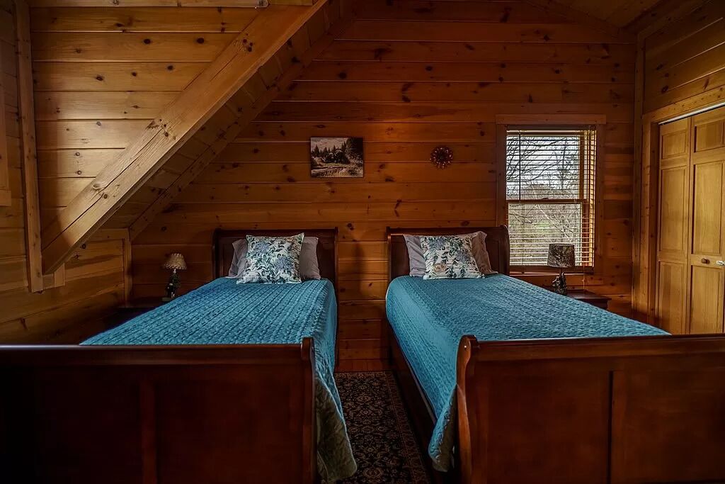 Una habitación acogedora con dos camas de madera, una ventana con persianas y una pequeña mesa con una lámpara.