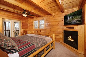 Ein Schlafzimmer in einer Blockhütte mit Bett, Kamin, Fernseher und Deckenventilator.