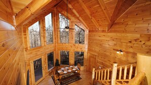 A spacious wooden cabin with a large dining table, a staircase, and multiple windows offering views of the surrounding forest. - Smoky Treehouse Lodge #614 (Sevierville)