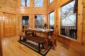Ein Holzhütten-Interieur mit Esstisch für vier Personen, großen Fenstern und Blick auf Bäume.