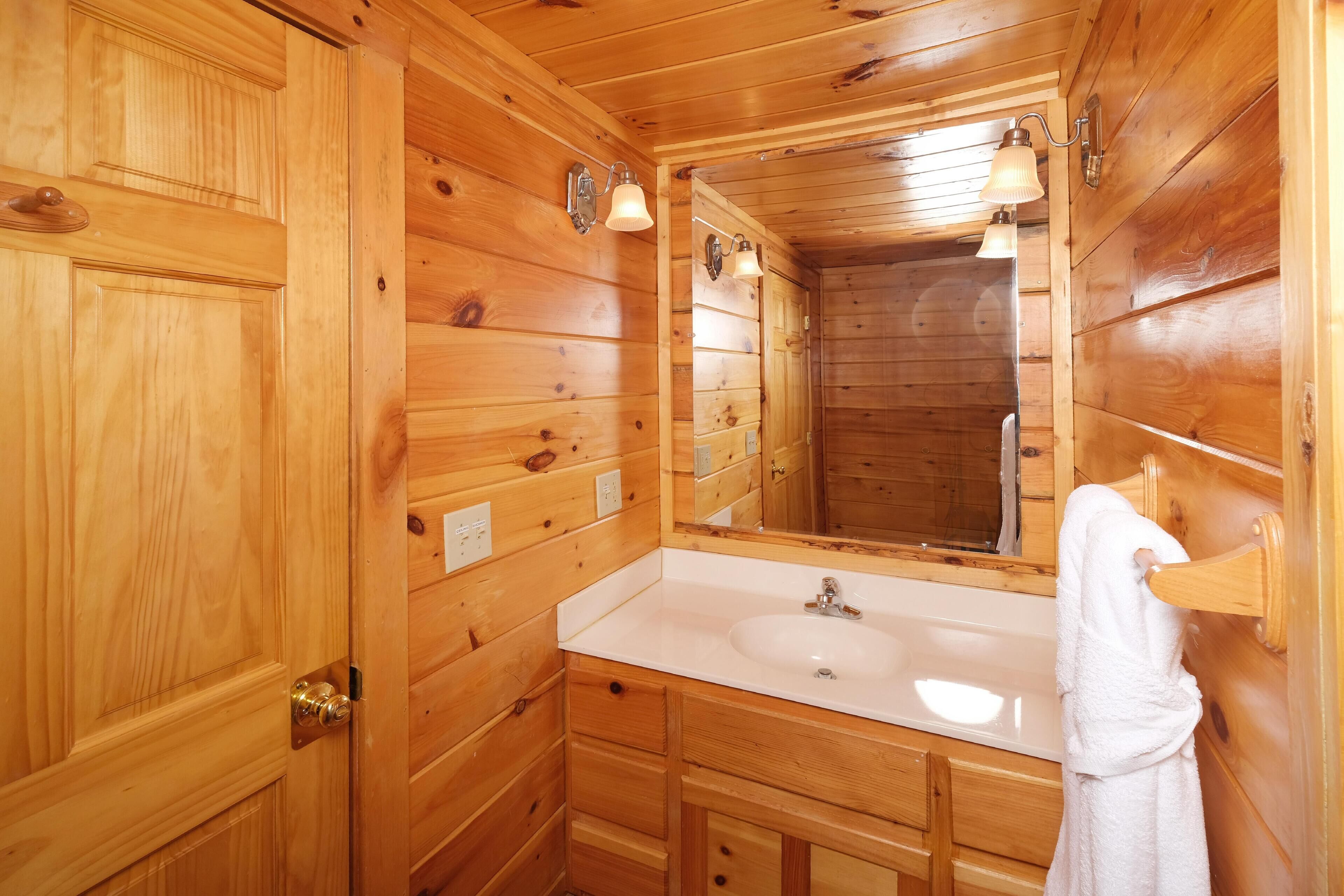 A wooden cabin-style bathroom with a large mirror, a sink, and a towel rack.