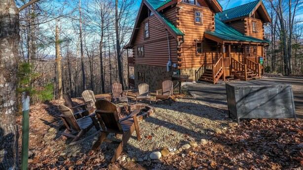 A log cabin with a stone foundation, wooden deck, and outdoor seating area with Adirondack chairs. - Smoky Treehouse Lodge #614 (Sevierville)