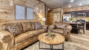 A cozy living room with a leather sofa, a wooden coffee table, and a kitchen area with dark wooden cabinets and modern appliances. - Sun Splash #342 (Sevierville)