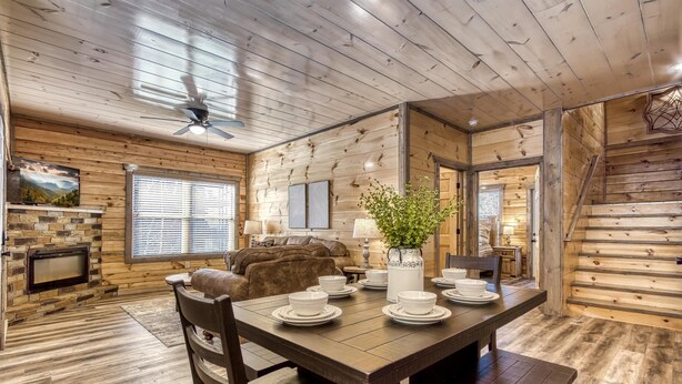A wooden interior with a dining table set for four, a fireplace, and a staircase. - Sun Splash #342 (Sevierville)