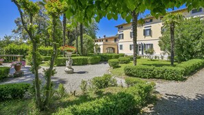 A courtyard with a gravel path, neatly trimmed hedges, and a building with multiple windows and balconies. - Tenuta Santa Colomba (Bientina)