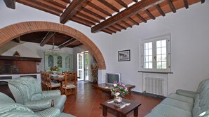 A spacious living area with a high ceiling, wooden beams, a dining area with a green cabinet, and a television. - Tenuta Santa Colomba (Bientina)