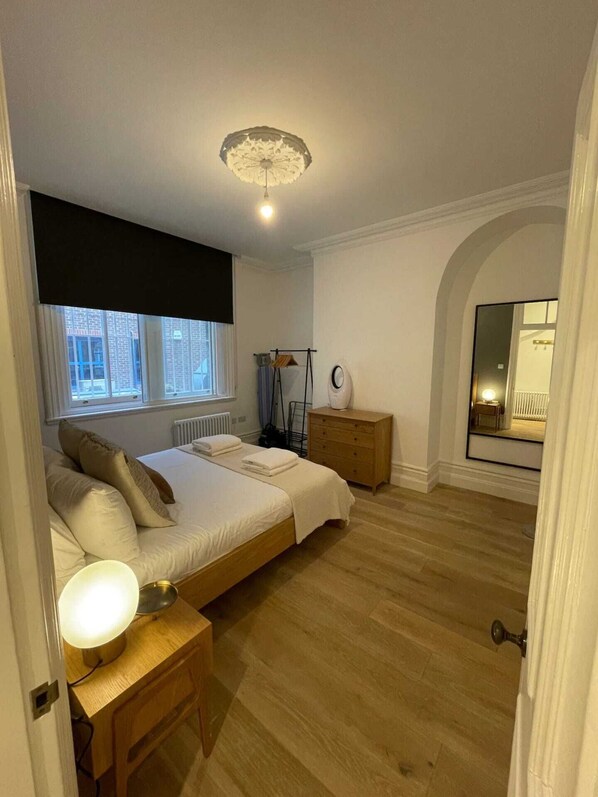 A bedroom with a bed, bedside tables, a radiator, a window, and a mirror.