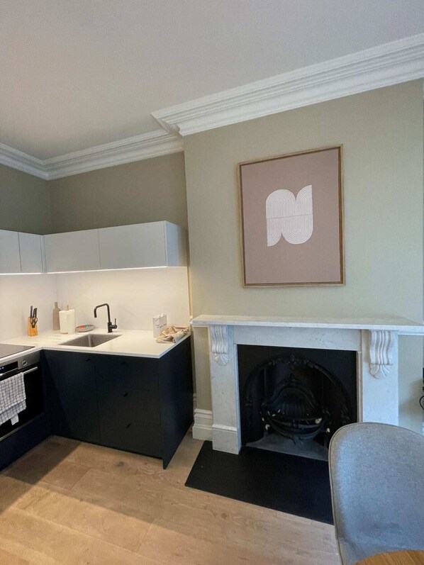A modern kitchen with a built-in island, a fireplace, and a framed artwork on the wall. - Central 1 Bedroom Apartment in Farringdon (London)