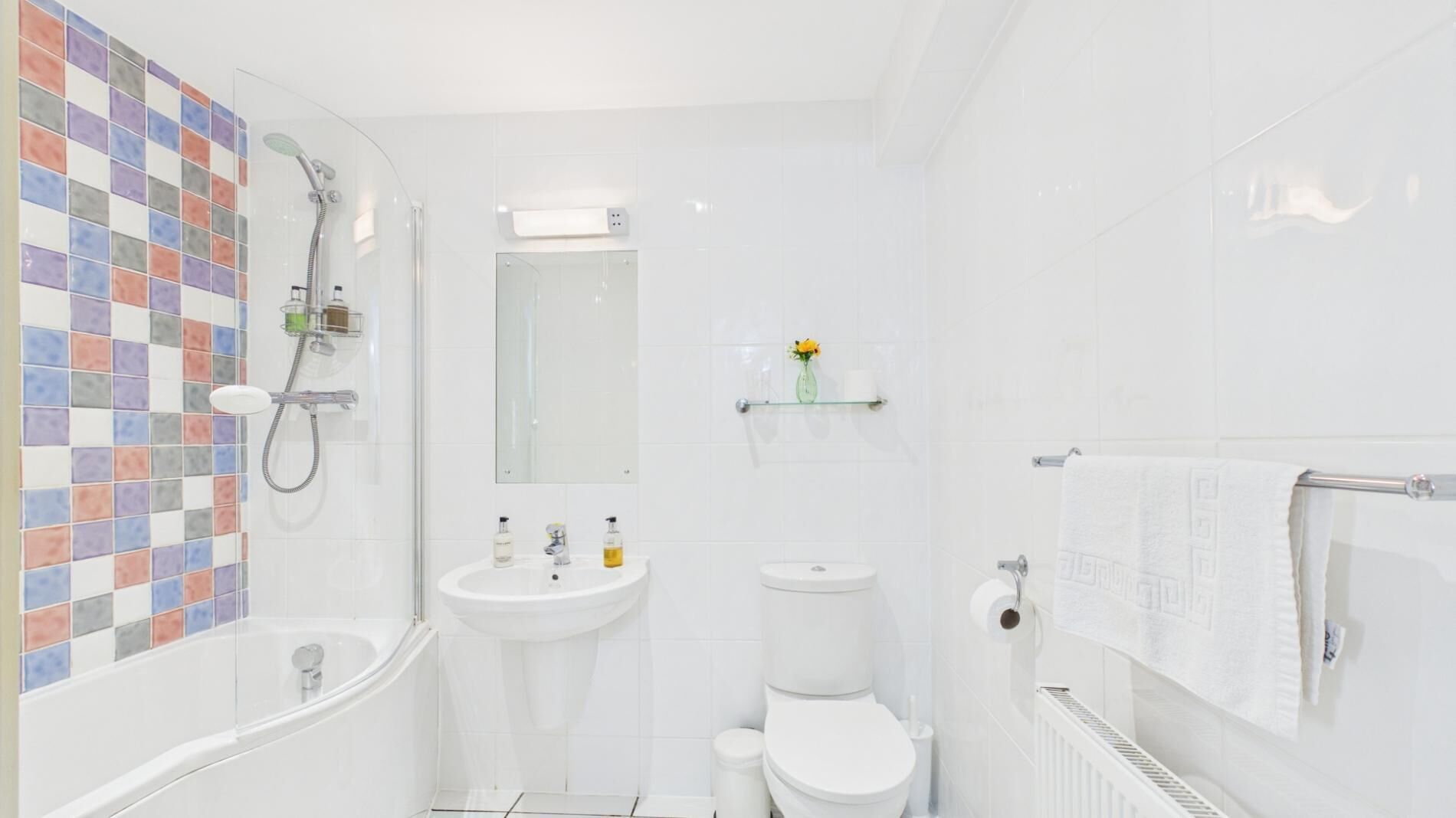 A bathroom with a tiled shower wall, a sink, a toilet, and a towel rack.