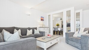 A modern living room with grey sofas, a white coffee table, and a dining area with a white table and chairs. - Minarvon - 2 Bedroom Apartment - Saundersfoot (Saundersfoot)