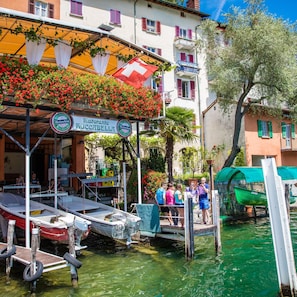 Un restaurante frente al agua con terraza, barcos amarrados cerca y vistas despejadas del mar.