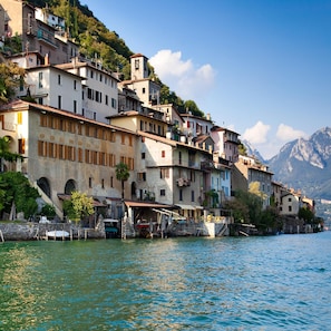 A waterfront building with multiple balconies and a tower, surrounded by water and mountains.