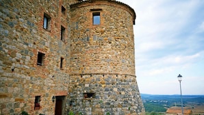 A stone tower with a circular base and a flat top, surrounded by a stone building with multiple windows and a red awning.