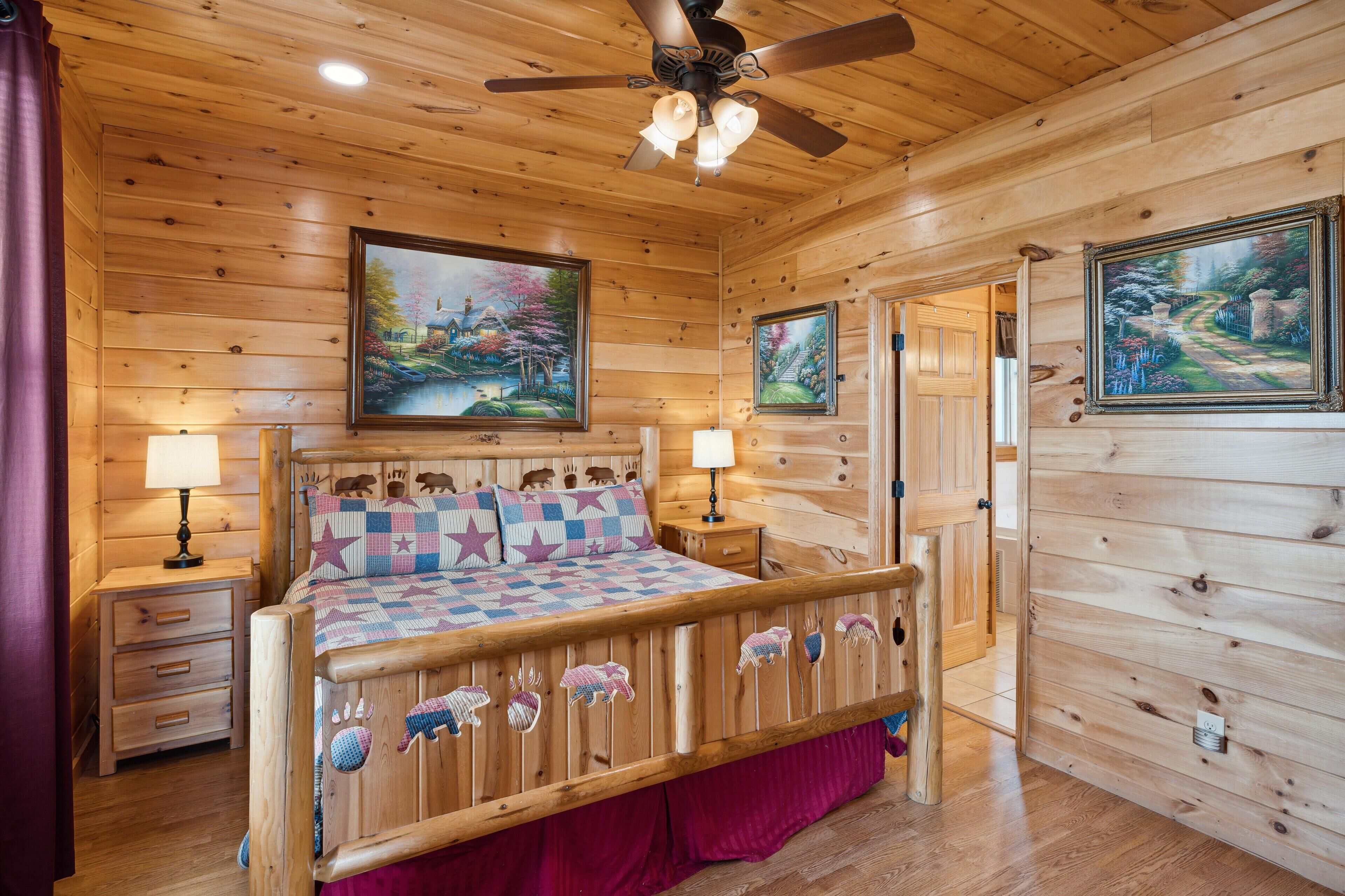 A wooden cabin bedroom with a bed, two nightstands, a ceiling fan, and two paintings on the walls.