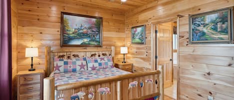 A wooden cabin bedroom with a bed, two nightstands, a ceiling fan, and two paintings on the walls.