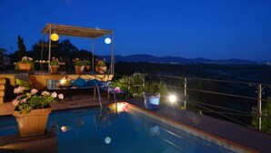 A pool area with a pergola, potted plants, and a view of the mountains at dusk. - Torre Del Melograno With Heated Pool (Castiglione in Teverina)