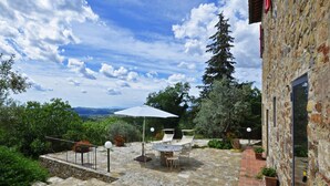 A stone patio with a table and chairs, an umbrella, and a view of the landscape.