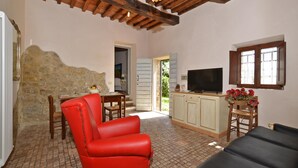 A cozy living room with a red chair, a black sofa, a television, and a stone wall.